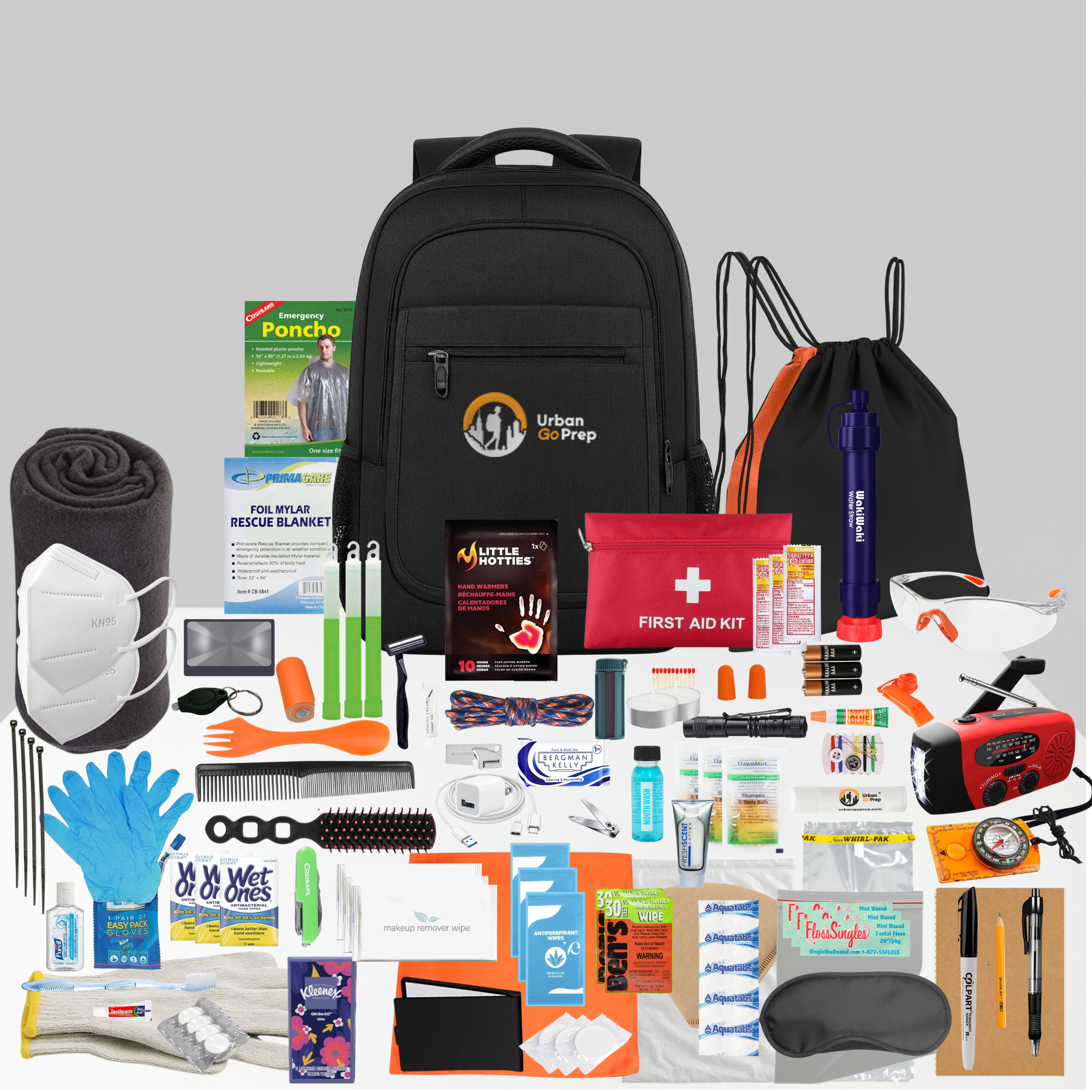 Collection of emergency supplies including a black backpack, first aid kit, face mask, and various other items on a gray background.
