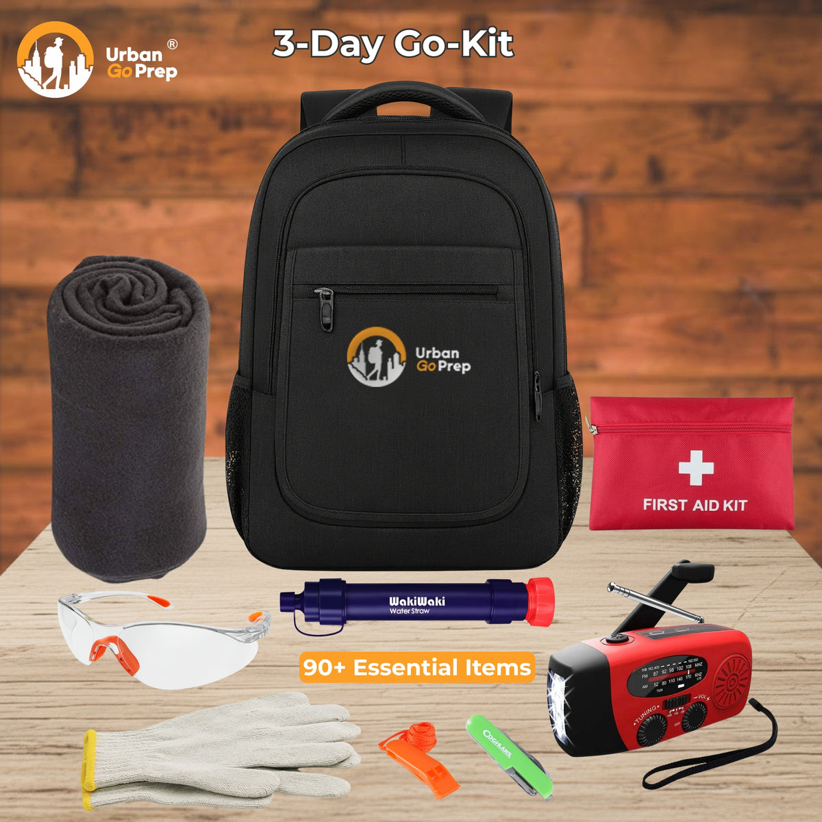 Urban Go Prep 3-Day Go-Kit laid out on a wooden surface with a wood plank background. The kit includes a black backpack, a rolled gray blanket, a red first aid kit pouch, a red-and-black portable radio, white safety glasses, white gloves, an orange whistle, a green first-aid patch, and a purple tourniquet, with text reading &