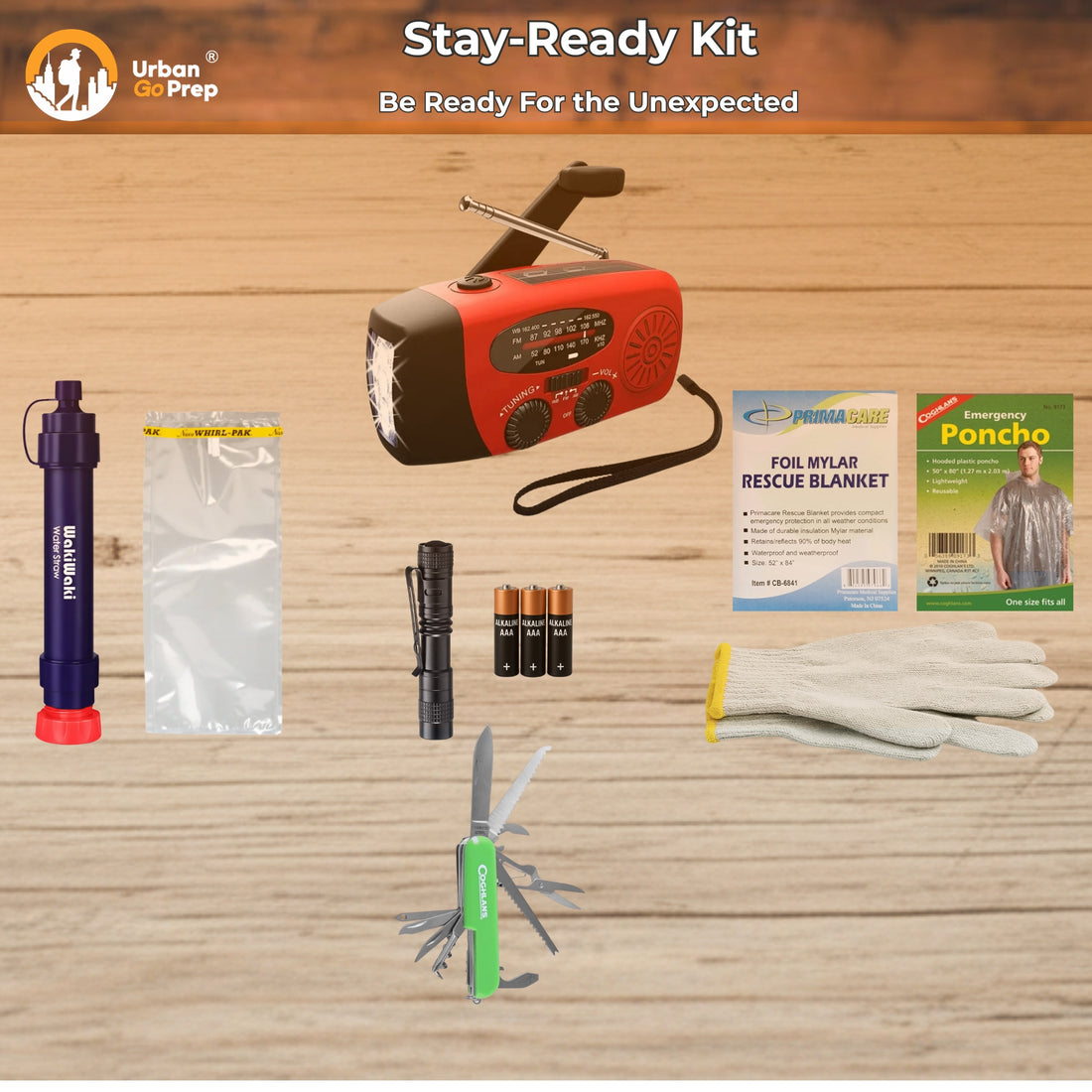 Urban Go Prep Stay-Ready Kit laid out on a light wood surface, including a red and black emergency radio, a blue pump, a plastic bag, a black flashlight, three batteries, a green multi-tool pocket knife, white gloves, a Poncho package, and a rescue blanket package.